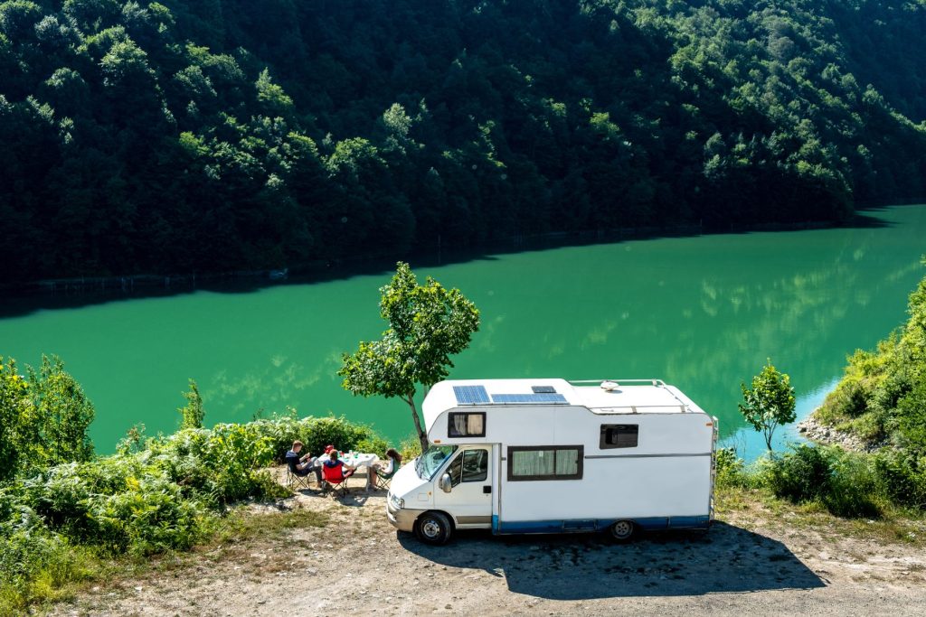 Family sits at a table outside overlooking a lake with their motorhome parked behind them